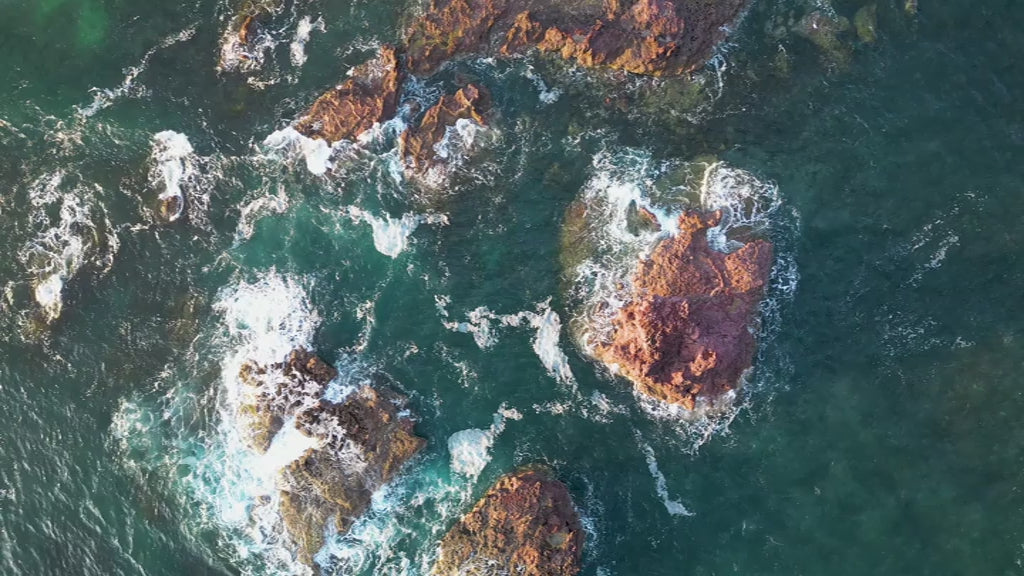 Aerial top-down view of large rocks waves crashing in green sea