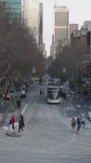 Classic green melbourne tram moving through a busy city street with modern trams, cars, and pedestrians during a daily commute