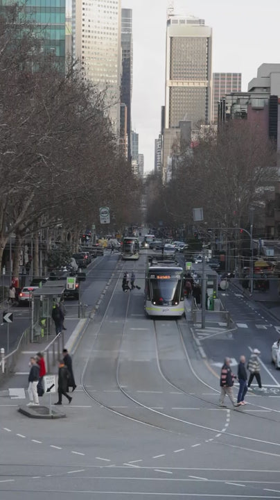 Classic green melbourne tram moving through a busy city street with modern trams, cars, and pedestrians during a daily commute