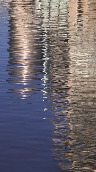 Abstract and calming background of a Gold metallic building reflecting on the serene, rippling surface of blue water, creating gentle shimmering waves