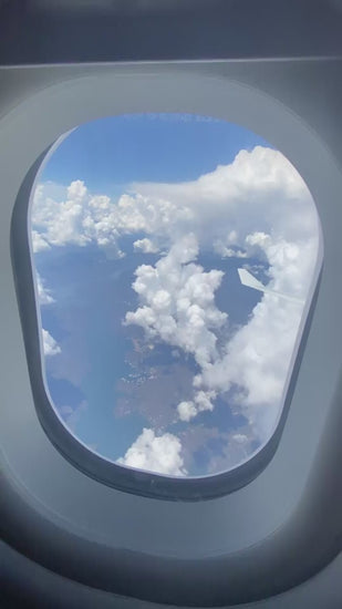 Beautiful view from an airplane window, looking down at white fluffy clouds, the blue ocean, and a distant coastline on a sunny day