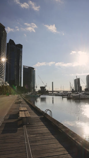 Wooden pier extending along Yarra River with blue sky, capturing Melbourne skyline reflecting on calm waters with vibrant urban landscape