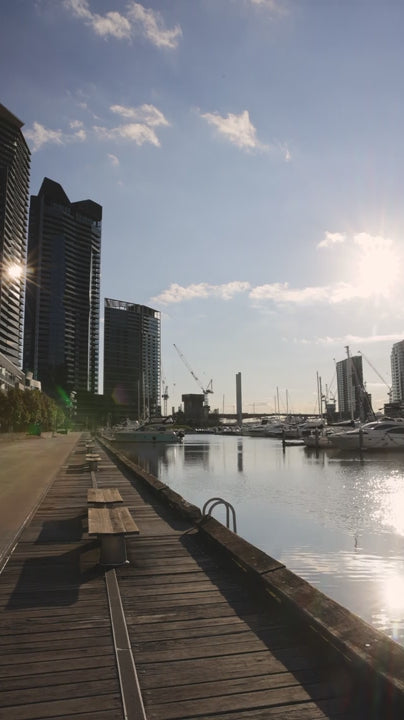Wooden pier extending along Yarra River with blue sky, capturing Melbourne skyline reflecting on calm waters with vibrant urban landscape