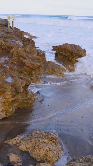 Soft golden sunlight illuminating gentle waves washing over rocky coastline in slow motion, creating serene morning seascape with tranquil ocean rhythms