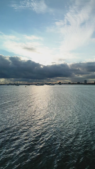 Aerial fly up reveal calm water with boats at St Kilda marina and Melbourne city skyline at sunset