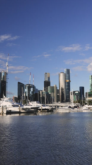 Melbourne skyline reflecting on over marina at Docklands with moored yachts and construction cranes in the background