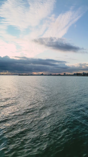 Darkening clouds veiling melbourne skyline, golden sunset reflecting across rippled waters near port phillip bay