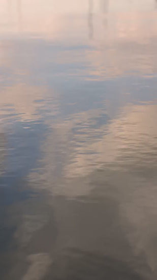 Tranquil water surface gently rippling and reflecting a beautiful, pastel pink and blue colorful sky. Peaceful and meditative natural background for relaxation