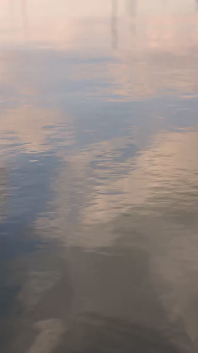 Tranquil water surface gently rippling and reflecting a beautiful, pastel pink and blue colorful sky. Peaceful and meditative natural background for relaxation