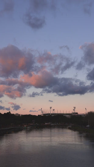 Melbourne Yarra River with sports stadium in background at pink and blue dusk with puffy clouds