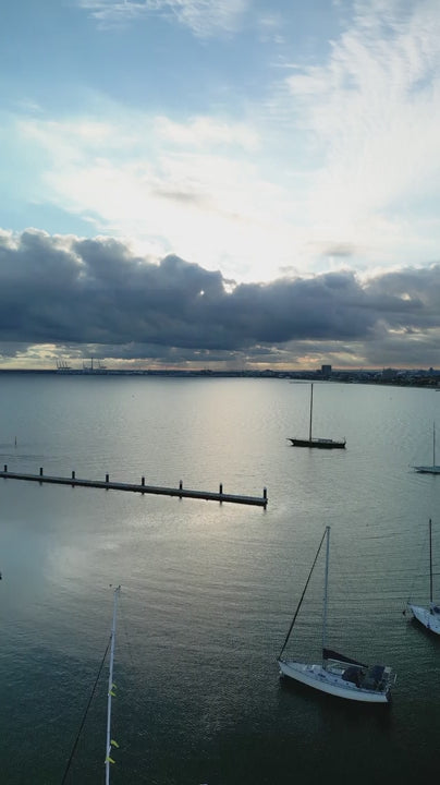 Aerial of Sailboat and pier out to ocean in Melbourne's Port Phillip Bay on cloudy day at sunset