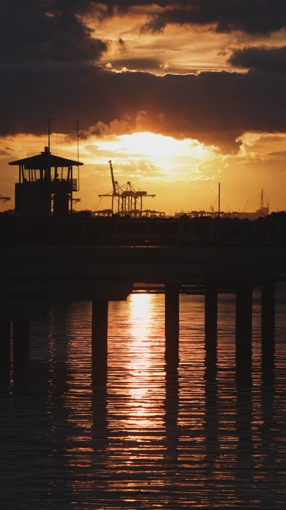 Golden sunset over calm water in slow motion with pier and cranes in silhouette in Melbourne
