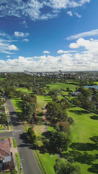 Aerial of Melbourne golf course exhibits its lush greenery under a vibrant blue sky dotted with fluffy white clouds - fly over