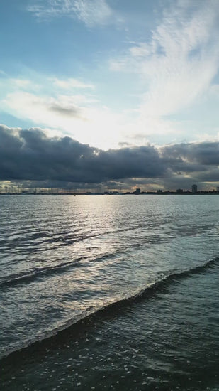 Calm waves lapping against shore reflecting sunlight on a cloudy skyline at sunset near St Kilda for a serene seascape
