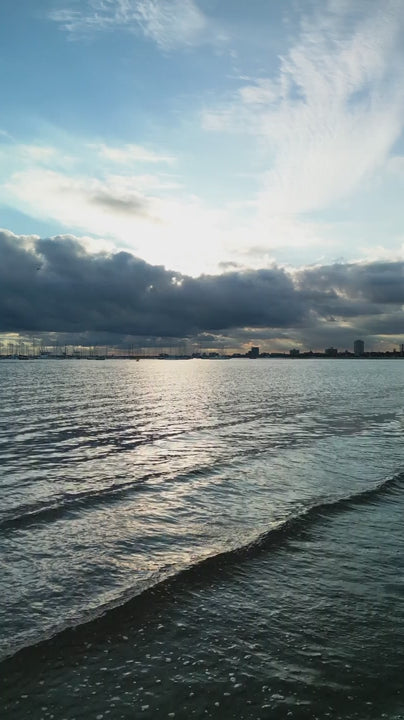 Calm waves lapping against shore reflecting sunlight on a cloudy skyline at sunset near St Kilda for a serene seascape