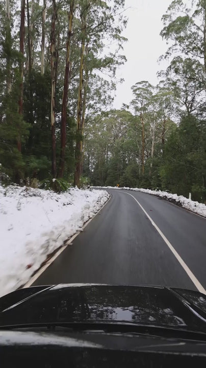 Point of view of Black car driving on snowy mountain road in Australia, showcasing serene winter landscape during scenic driving journey