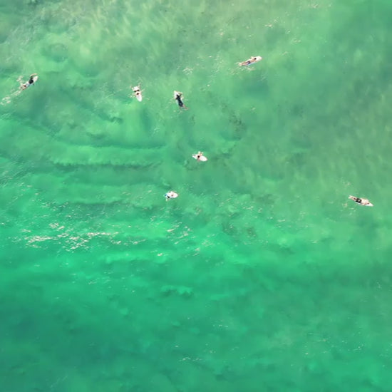Top-down aerial view of surfers catching a wave on the Gold Coast