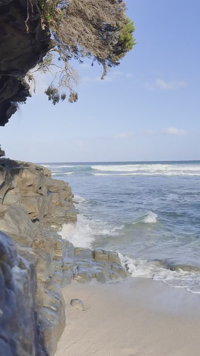 Tranquil coastal scene showing calm ocean waves washing ashore on a sandy beach next to a rocky cliff. A beautiful, serene nature background